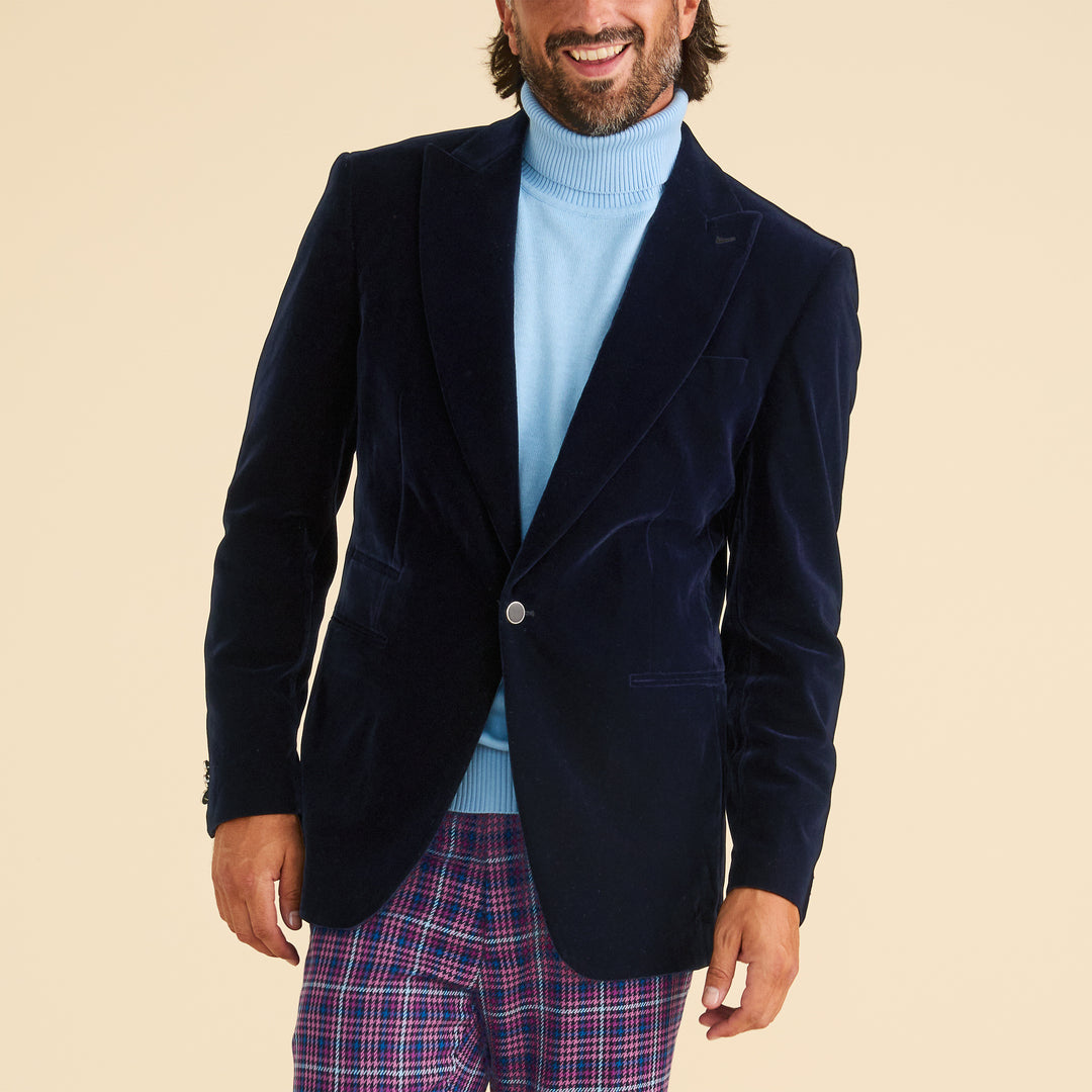 A person smiles against a plain light background, wearing the Inserch Velvet Blazer BL007-11 Navy Blue by Inserch, paired with a light blue turtleneck sweater and plaid pants.