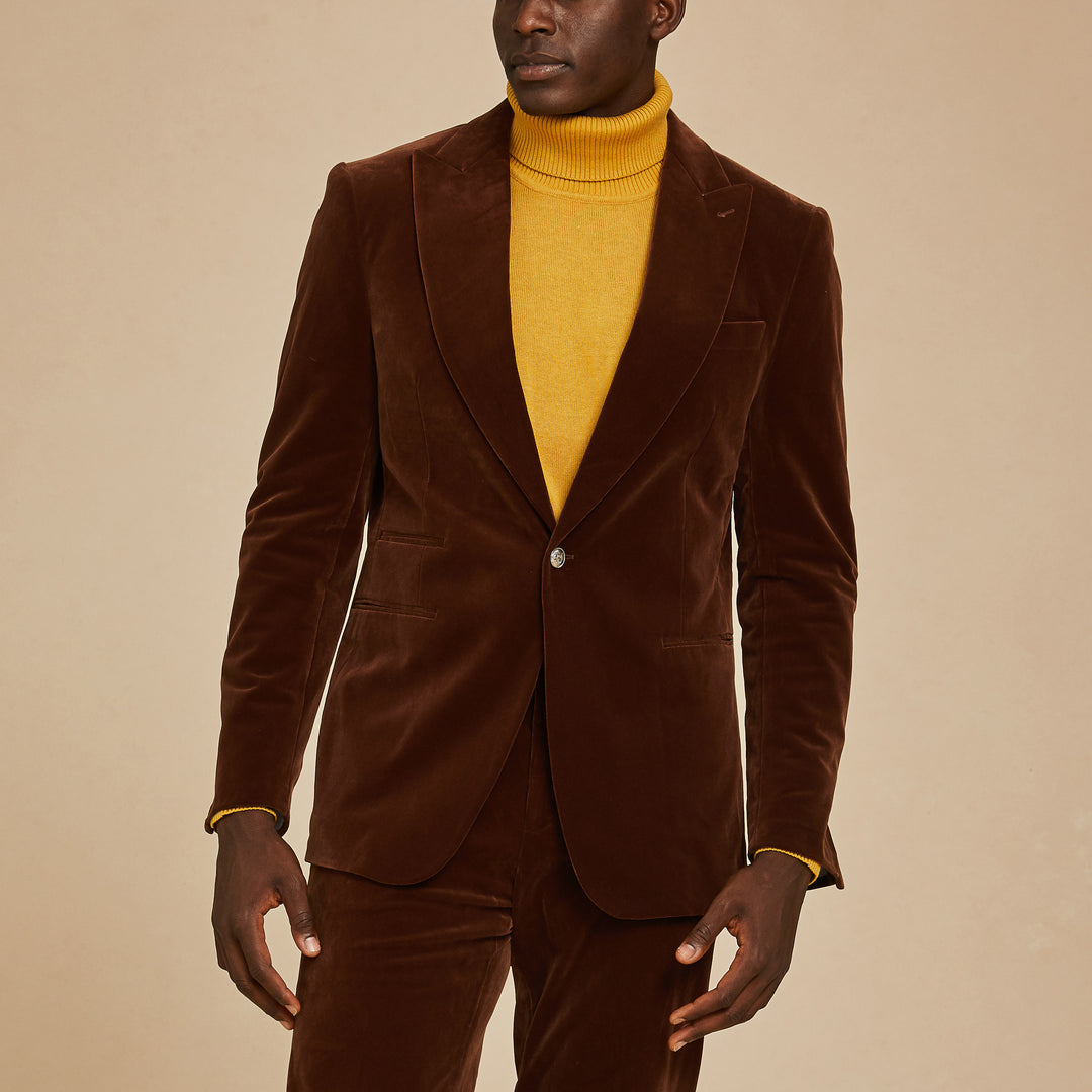 A person wearing the Inserch Velvet Blazer BL007-131 Swiss Chocolate by Inserch with matching pants over a mustard yellow turtleneck, standing against a beige background.