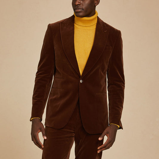 A person wearing the Inserch Velvet Blazer BL007-131 Swiss Chocolate by Inserch with matching pants over a mustard yellow turtleneck, standing against a beige background.