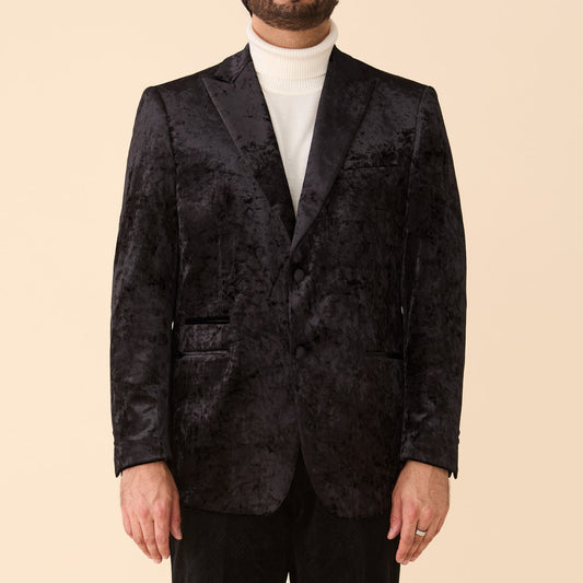 A man wearing the Inserch Crushed Velvet Suit BL008-00001 Black over a white turtleneck and modern fit pants, standing against a plain beige background.