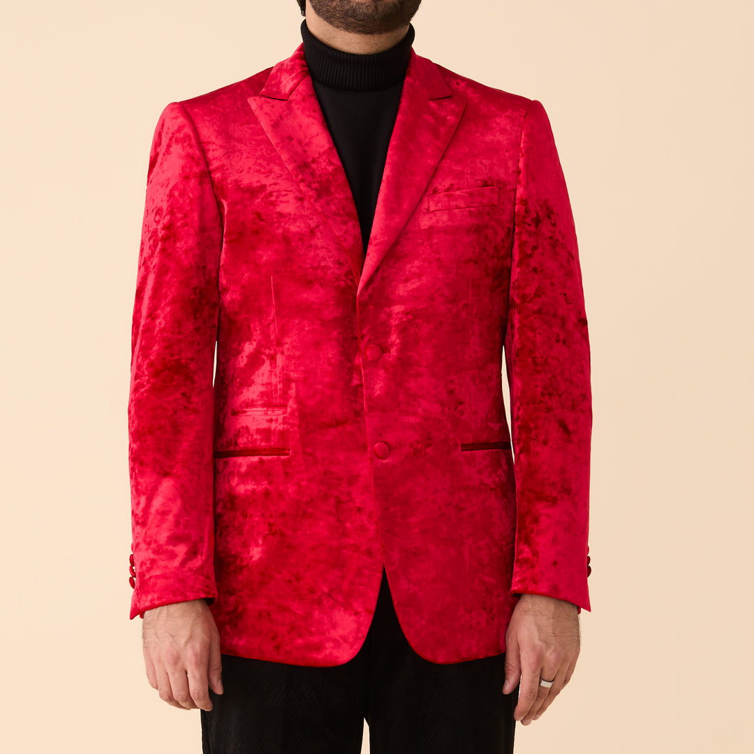 A man wearing the Inserch Crushed Velvet Blazer BL008-00030 Red by Inserch over a black turtleneck and black pants stands against a beige background.