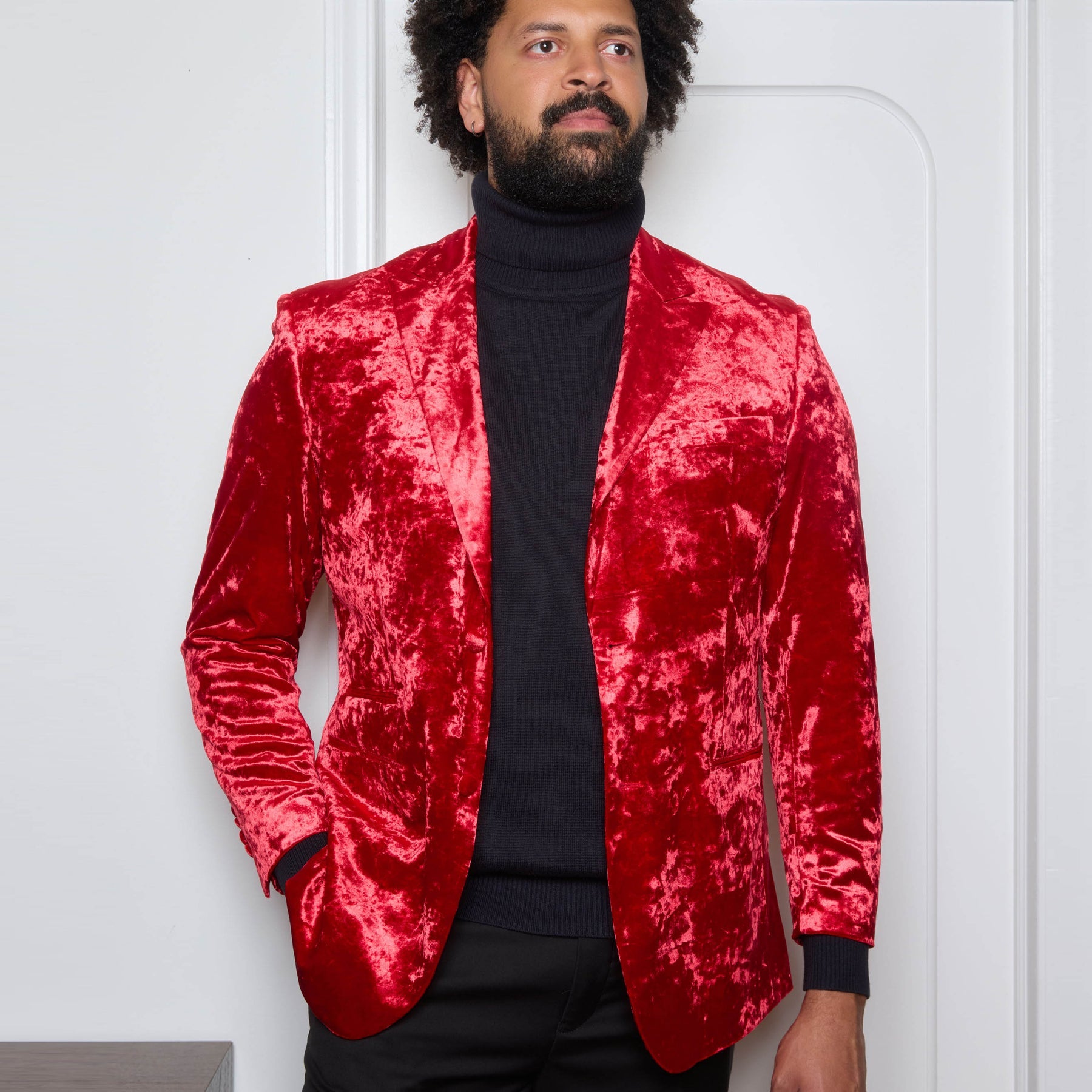 A man wearing the Inserch Crushed Velvet Blazer BL008-00030 Red by Inserch over a black turtleneck and black pants stands against a beige background.