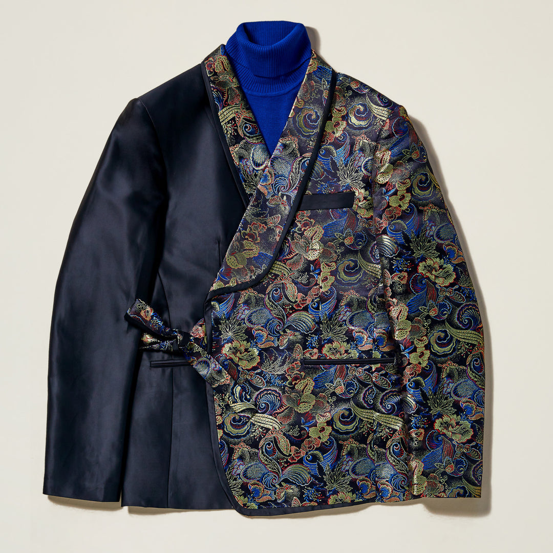 The Inserch Tied Floral Blazer BL207-01 Black by Inserch features a slim fit, with one side in solid black satin and the other in vibrant floral jacquard, finished with a sleek shawl collar and styled over a royal blue turtleneck.