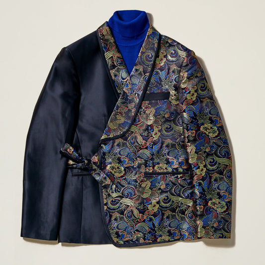 The Inserch Tied Floral Blazer BL207-01 Black by Inserch features a slim fit, with one side in solid black satin and the other in vibrant floral jacquard, finished with a sleek shawl collar and styled over a royal blue turtleneck.
