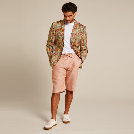 A man stands against a plain backdrop wearing the Inserch Patchwork Print Blazer BL261-35 Rust by Inserch, paired with a white t-shirt, pink shorts, and white sneakers.