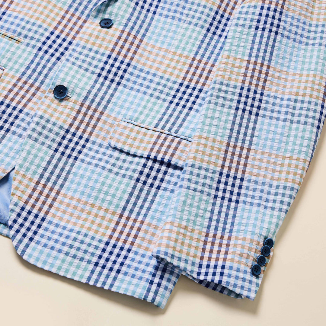 A man wears the Inserch Cotton Seersucker Check Blazer BL262-00066 Multi with an orange sweater, blue trousers, and brown dress shoes against a beige background. His head is not visible in the image. Brand: Inserch.