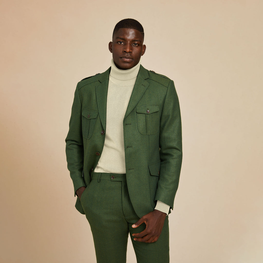 A man stands against a plain beige background wearing the Inserch Herringbone Blazer BL263-19 Olive by Inserch, paired with a light-colored turtleneck sweater and one hand in his pocket.