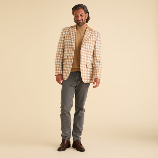 A man stands against a beige background wearing the Inserch Houndstooth Blazer BL264-09 Khaki by Inserch, paired with a tan turtleneck, gray jeans, and brown shoes.