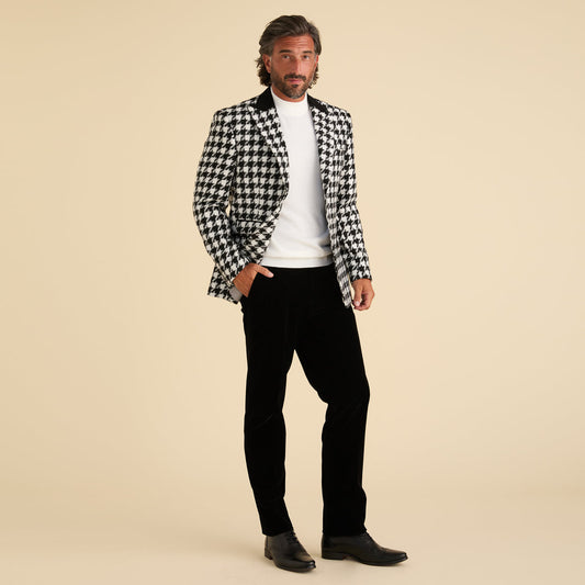 A man stands against a plain background wearing the Inserch Houndstooth Blazer BL264-41 Black/White, paired with a white sweater, black pants, and black dress shoes—the sharp peak lapel adds a modern edge to his sophisticated style.