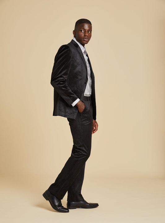 A man poses against a beige background wearing the Inserch Suede Snake Skin Blazer BL268-01 Black with a light dress shirt and black shoes, one hand in his pocket.