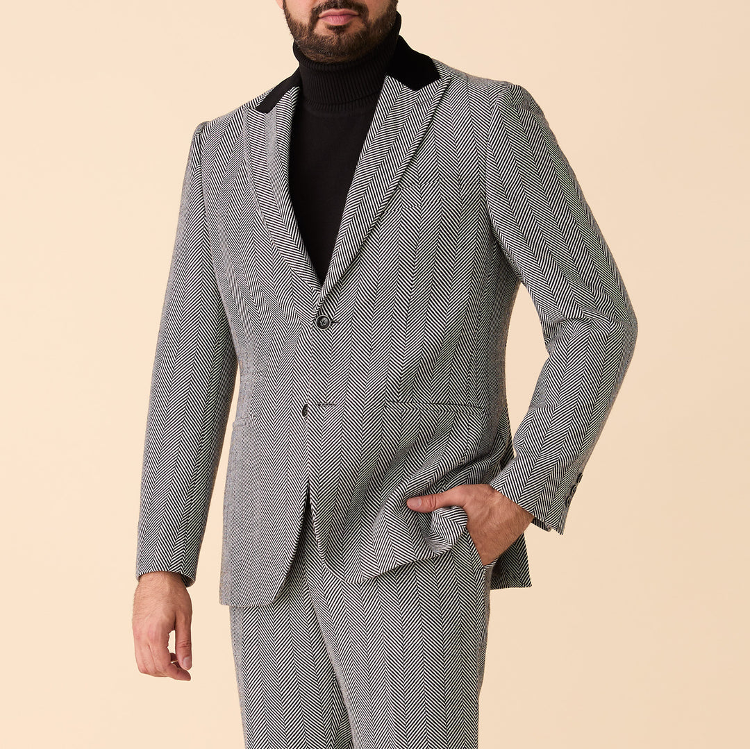 A man wearing the Inserch Herringbone Blazer BL273-00041 in Black/White by Inserch with a black turtleneck poses against a beige background, one hand in his pocket.