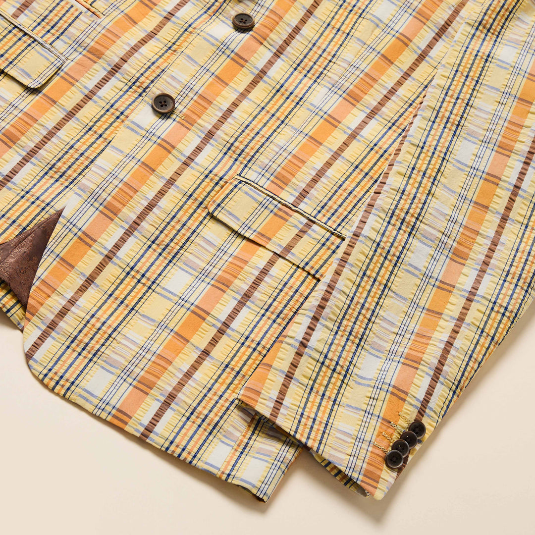 A man wearing the Inserch Seersucker Check Blazer BL277-00055 Yuzu by Inserch, paired with a brown shirt and yellow pants, stands against a beige background.