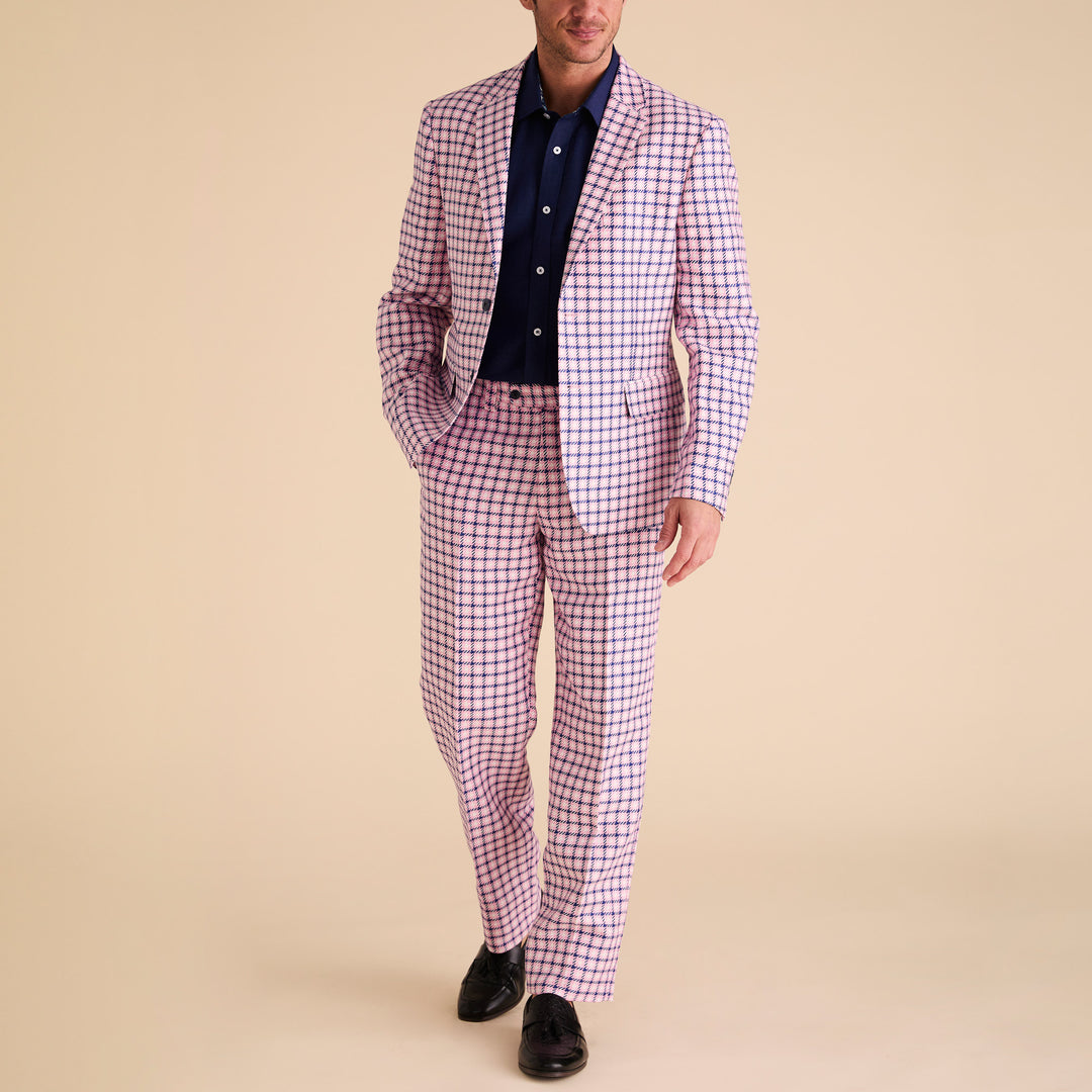 A man in a white shirt and pink plaid, Inserch Houndstooth Linen Blazer BL279-00062 Pink, featuring a subtle houndstooth pattern with a classic notch collar, holds the lapel. Posing against a plain white backdrop, he pairs it elegantly with light pink pants for sophistication.