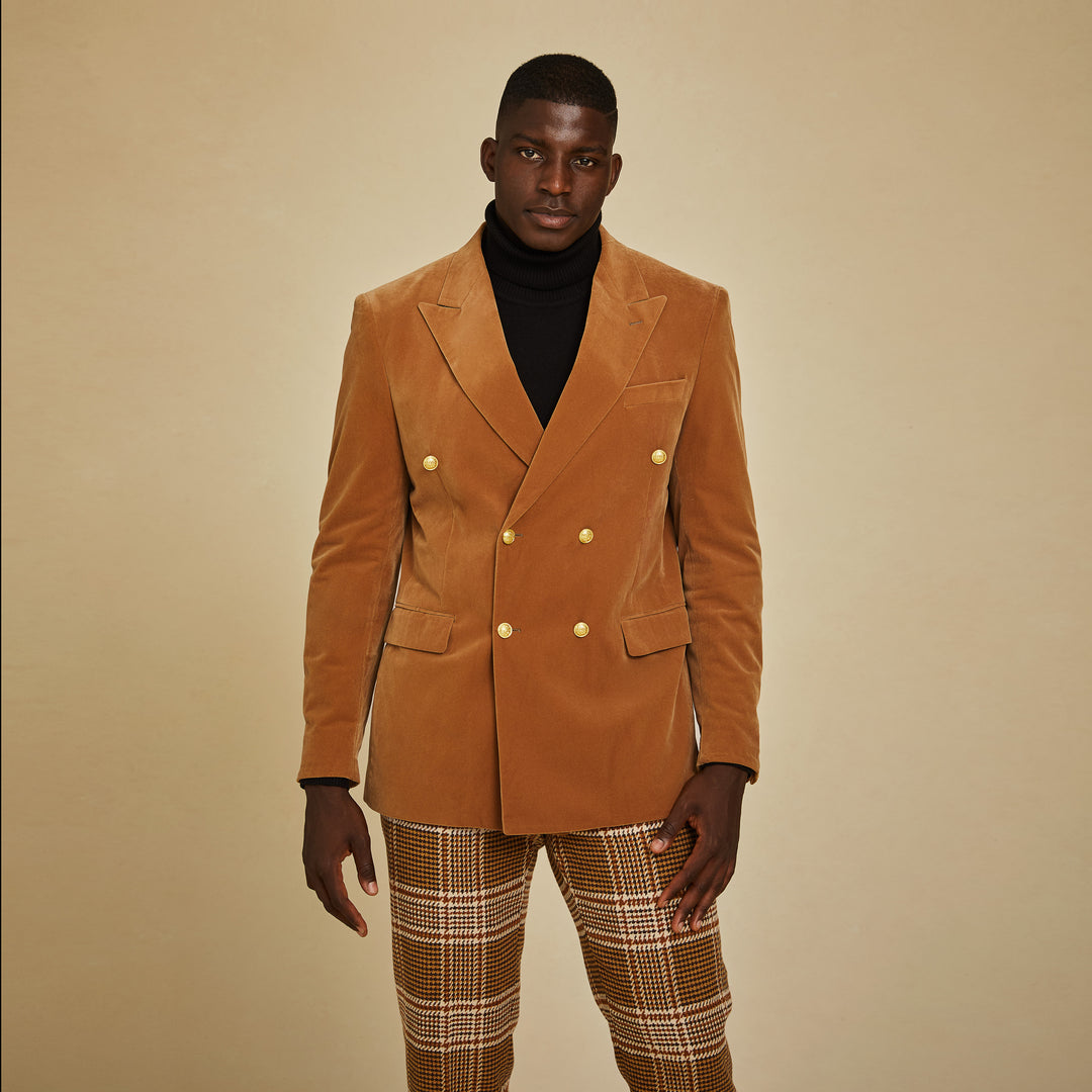 A man stands against a beige background wearing the Inserch DB Velvet Blazer BL502-184 Brown Sugar, paired with a black turtleneck and plaid pants.