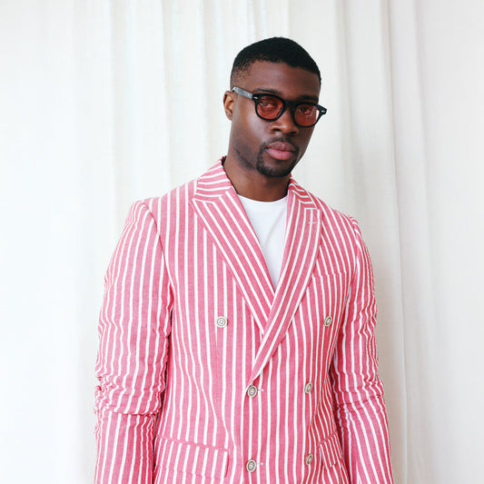 A person stands against a plain beige background, wearing the Inserch Seersucker Wide Stripe Blazer BL507-00030 in red with a crisp white shirt and brown shoes, subtly complemented by gingham check accents.