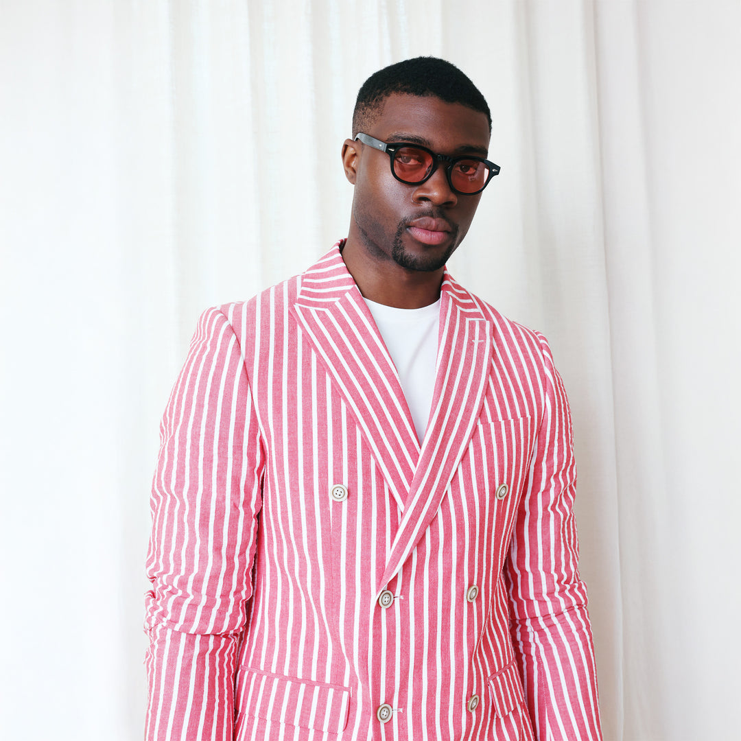 A man wears the Inserch Seersucker Wide Stripe Suit BL507-00030 Red by Inserch, paired with a white shirt and brown dress shoes, standing against a beige background.