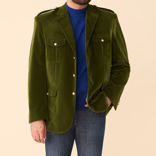 A man wears the Inserch Velvet Military Blazer BL569-19 Olive by Inserch over a blue turtleneck and blue jeans, standing against a beige background.