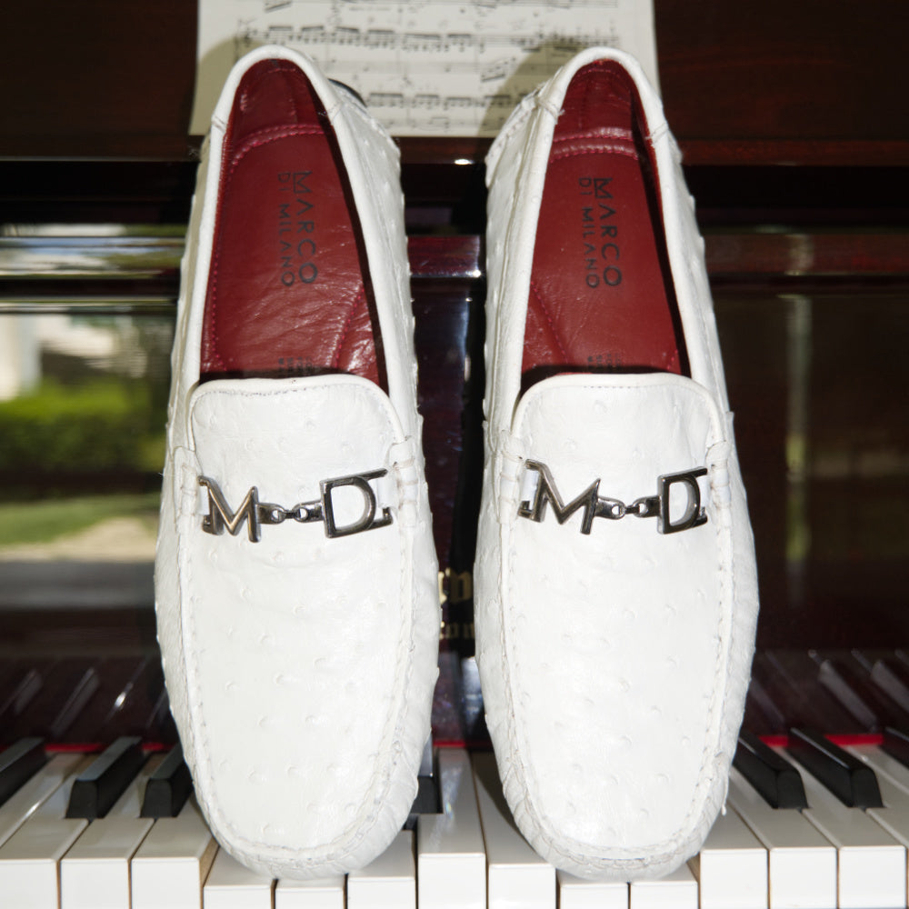 A pair of Bolonia White loafers by Marco Di Milano, featuring metal detailing on the front; one shoe stands upright while the other lies sideways to showcase the black and white sole—expertly crafted luxury moccasins designed to elevate any ensemble.