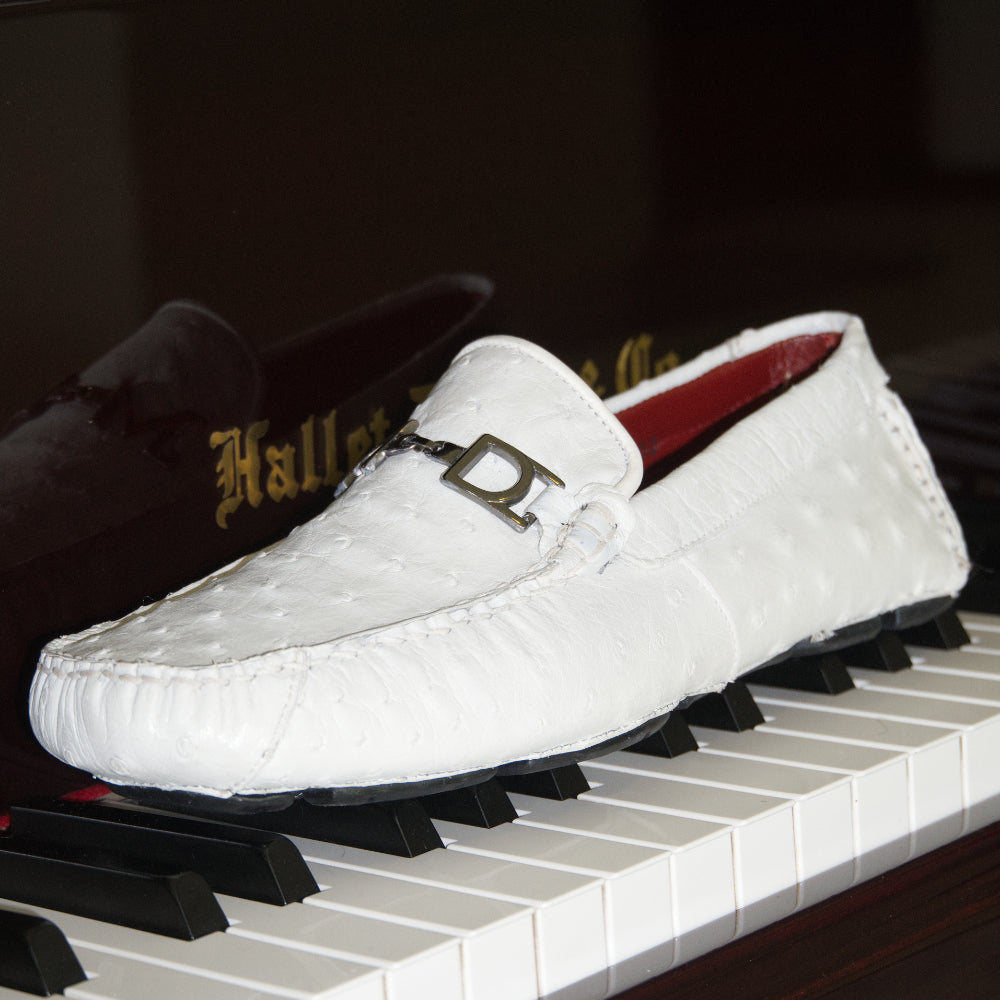 A pair of Bolonia White loafers by Marco Di Milano, featuring metal detailing on the front; one shoe stands upright while the other lies sideways to showcase the black and white sole—expertly crafted luxury moccasins designed to elevate any ensemble.