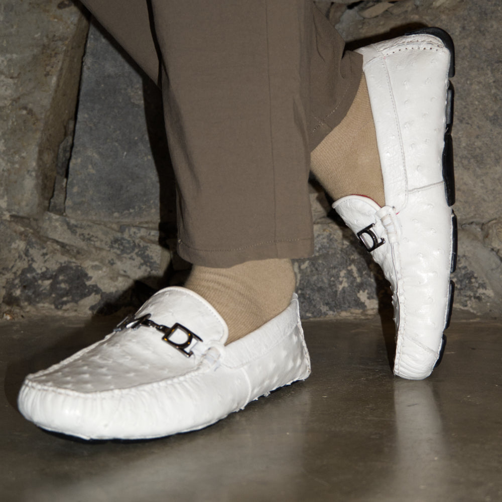 A pair of Bolonia White loafers by Marco Di Milano, featuring metal detailing on the front; one shoe stands upright while the other lies sideways to showcase the black and white sole—expertly crafted luxury moccasins designed to elevate any ensemble.