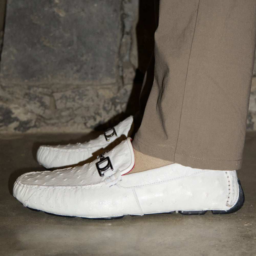 A pair of Bolonia White loafers by Marco Di Milano, featuring metal detailing on the front; one shoe stands upright while the other lies sideways to showcase the black and white sole—expertly crafted luxury moccasins designed to elevate any ensemble.