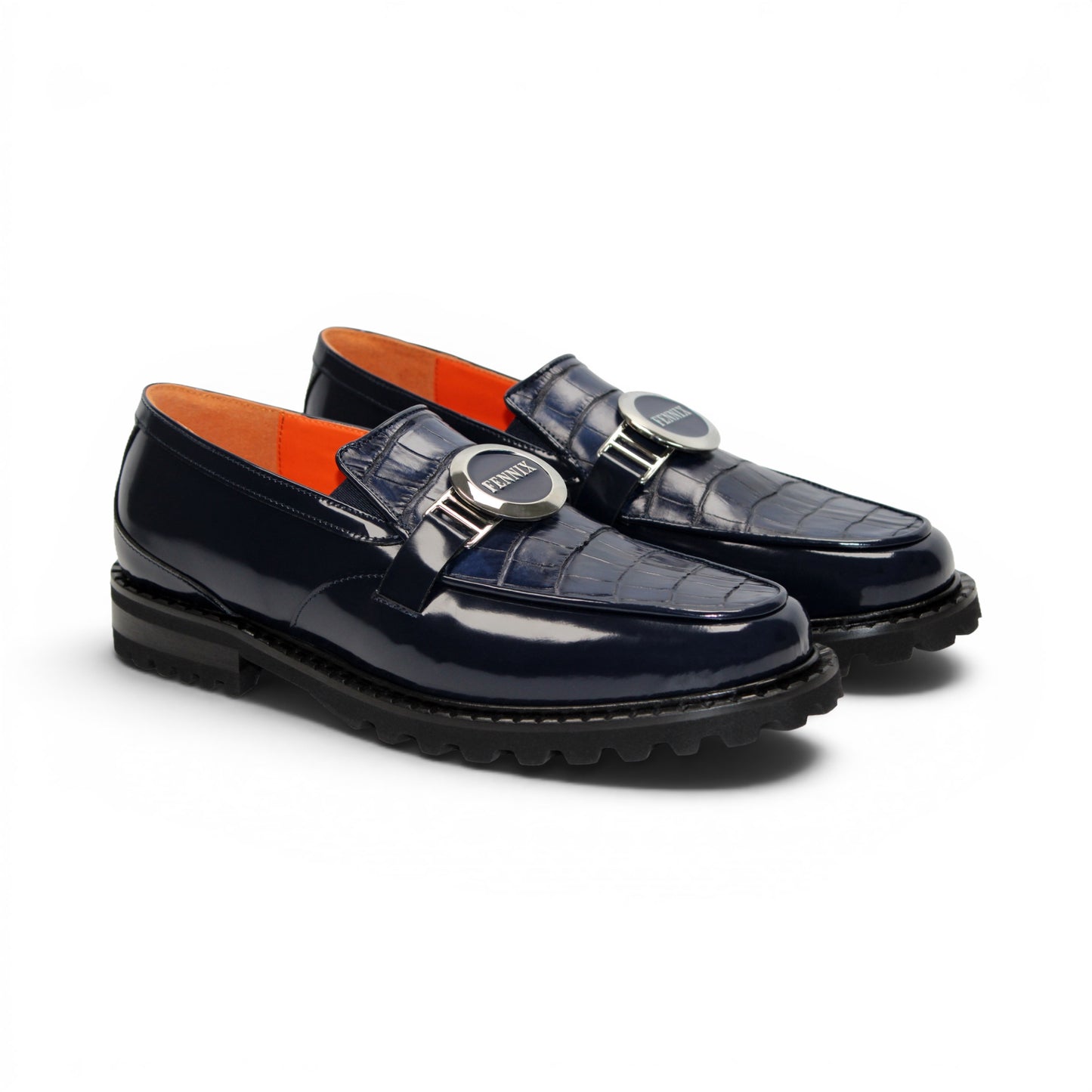 Introducing the Fennix Brant Navy from Fennix of Italy—a sleek navy blue loafer featuring a chunky black sole, vibrant orange inner lining, and a silver buckle accent across the upper strap. Expertly crafted in Italy, this shoe blends contemporary flair with classic elegance.