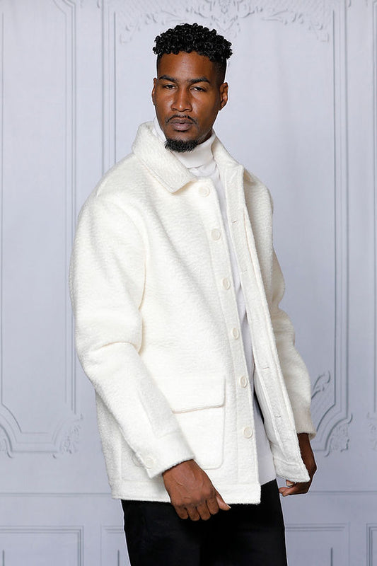 A man in the MANZINI CANADA White Short Ripple Faux Fur Button Coat by Insomnia stands against a white paneled background, looking to the side.