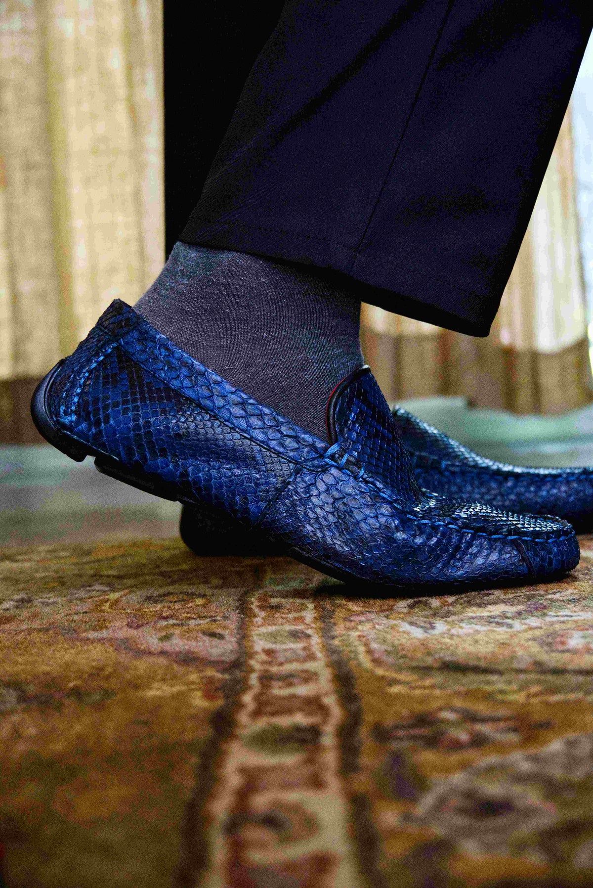 A pair of Capri Blue Jeans loafers by Marco Di Milano, crafted with a striking blue snakeskin texture; one shoe stands upright while the other lies on its side to reveal the black rubber sole—an elegant display of handcrafted luxury for those seeking exquisite exotic footwear.