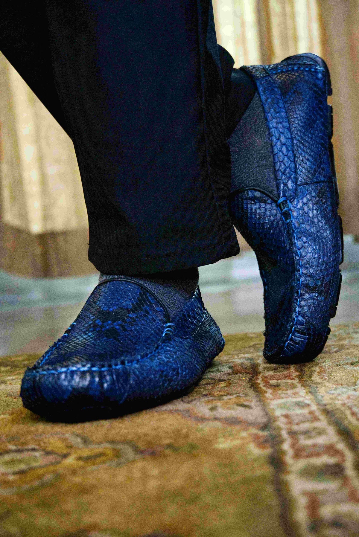 A pair of Capri Blue Jeans loafers by Marco Di Milano, crafted with a striking blue snakeskin texture; one shoe stands upright while the other lies on its side to reveal the black rubber sole—an elegant display of handcrafted luxury for those seeking exquisite exotic footwear.