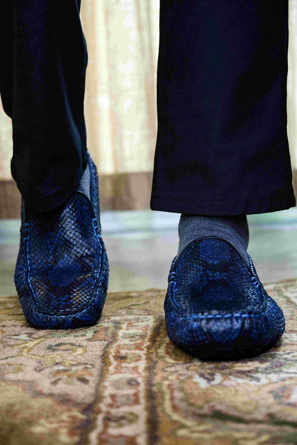 A pair of Capri Blue Jeans loafers by Marco Di Milano, crafted with a striking blue snakeskin texture; one shoe stands upright while the other lies on its side to reveal the black rubber sole—an elegant display of handcrafted luxury for those seeking exquisite exotic footwear.