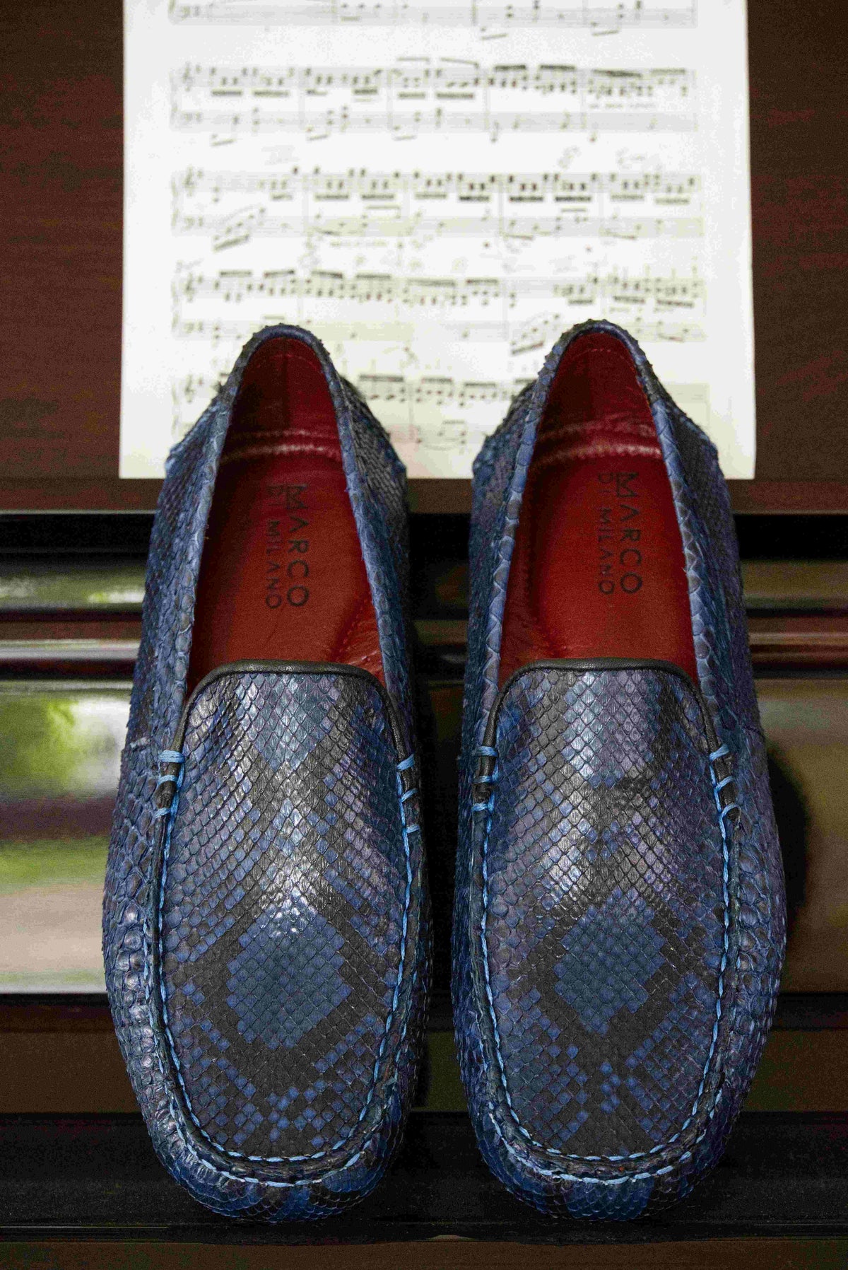 A pair of Capri Blue Jeans loafers by Marco Di Milano, crafted with a striking blue snakeskin texture; one shoe stands upright while the other lies on its side to reveal the black rubber sole—an elegant display of handcrafted luxury for those seeking exquisite exotic footwear.