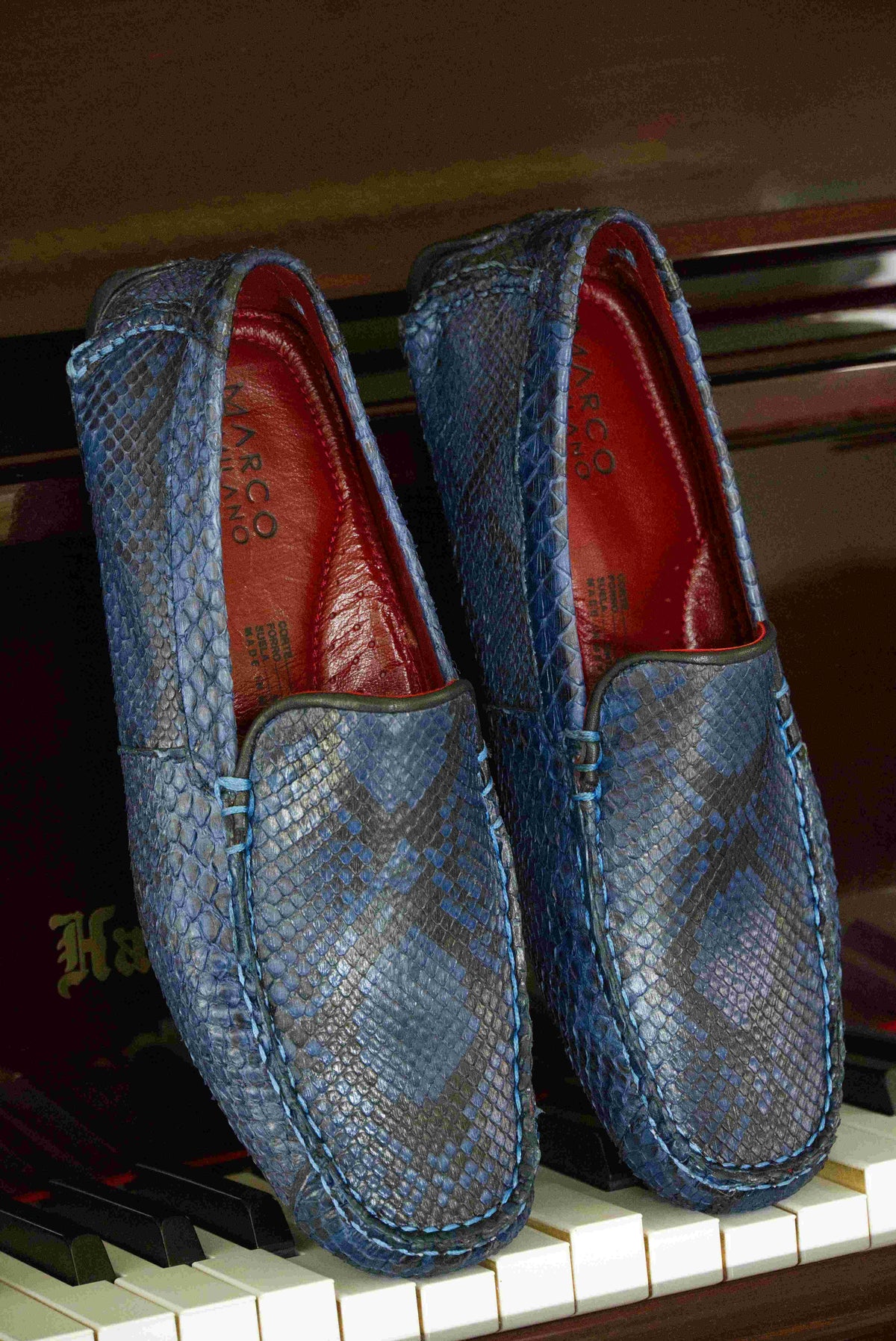 A pair of Capri Blue Jeans loafers by Marco Di Milano, crafted with a striking blue snakeskin texture; one shoe stands upright while the other lies on its side to reveal the black rubber sole—an elegant display of handcrafted luxury for those seeking exquisite exotic footwear.