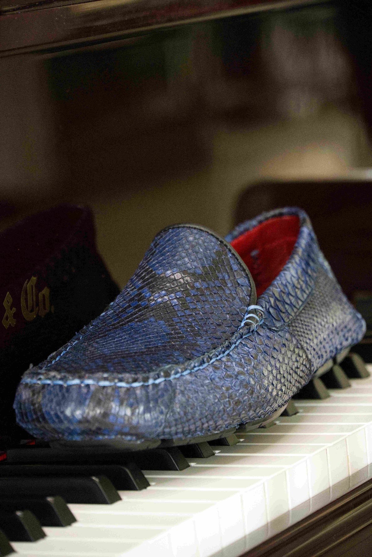 A pair of Capri Blue Jeans loafers by Marco Di Milano, crafted with a striking blue snakeskin texture; one shoe stands upright while the other lies on its side to reveal the black rubber sole—an elegant display of handcrafted luxury for those seeking exquisite exotic footwear.
