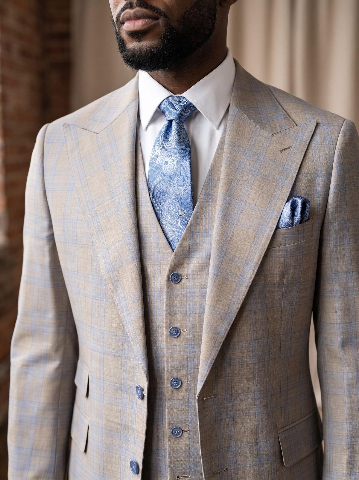 A man wearing a Tiglio Luxe Antibes Semi Tan/Blue Plaid Wide Leg Suit TL8312, a three-piece pure wool suit with a white dress shirt and blue paisley tie, embodying luxury men’s clothing.