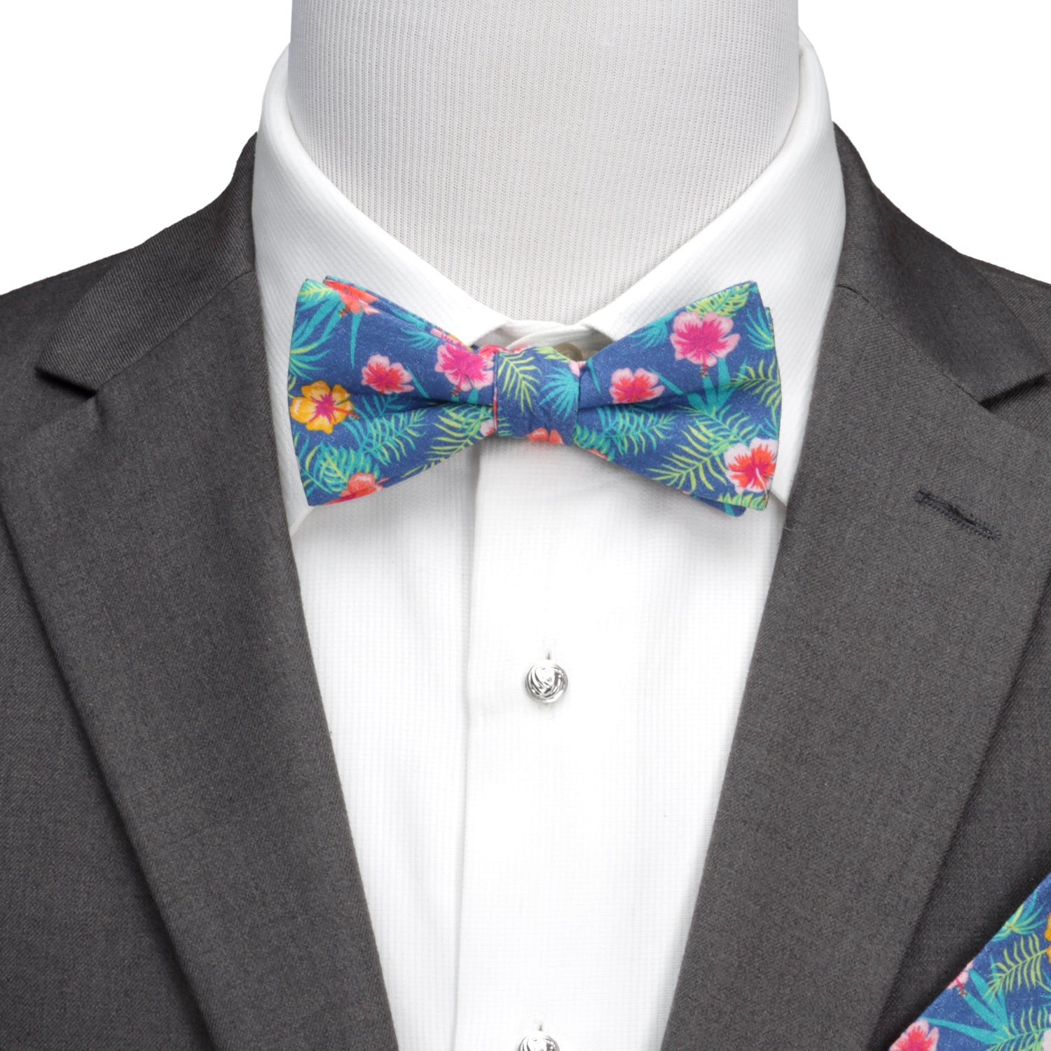The Tropical Multi Men’s Bow Tie by Cufflinks.com features a colorful floral pattern with pink, yellow, and red flowers, green palm leaves, and vibrant hibiscus accents.