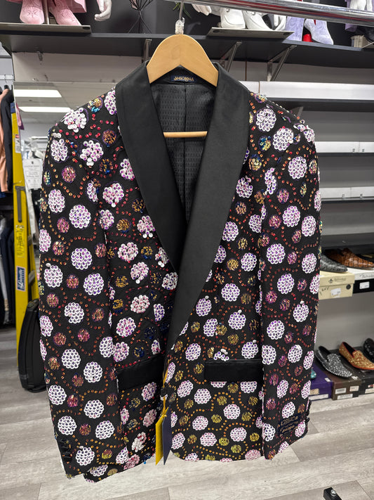The EJ SAMUEL JACKET 1 CLEARANCE, featuring a black base with a vibrant floral pattern and black satin lapels, hangs on a wooden hanger in the clothing store. Please note, this item is final sale—no exchanges or returns.