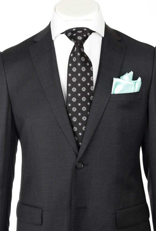 A mannequin showcases the CANALETTO PORTO Slim Fit, Charcoal Gray Pure Wool Suit by REDA Cloth CRS901, paired with a white shirt, black patterned tie, and light blue pocket square—an elegant example of luxury menswear.