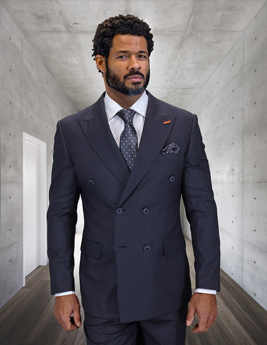 A bearded man in the STATEMENT CLOTHING | DB-SALOTE-BLACK modern fit, double-breasted Italian wool suit by Statement Clothing, white shirt, and patterned tie stands in a sleek concrete hallway.