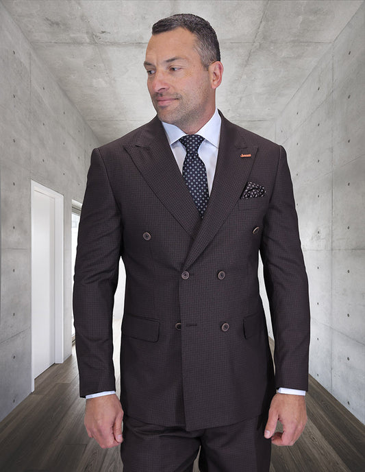 A man in a modern fit, double-breasted STATEMENT CLOTHING | DB-SALOTE-BROWN suit by Statement Clothing stands in a minimalist concrete hallway with a neutral expression, looking slightly to the side.