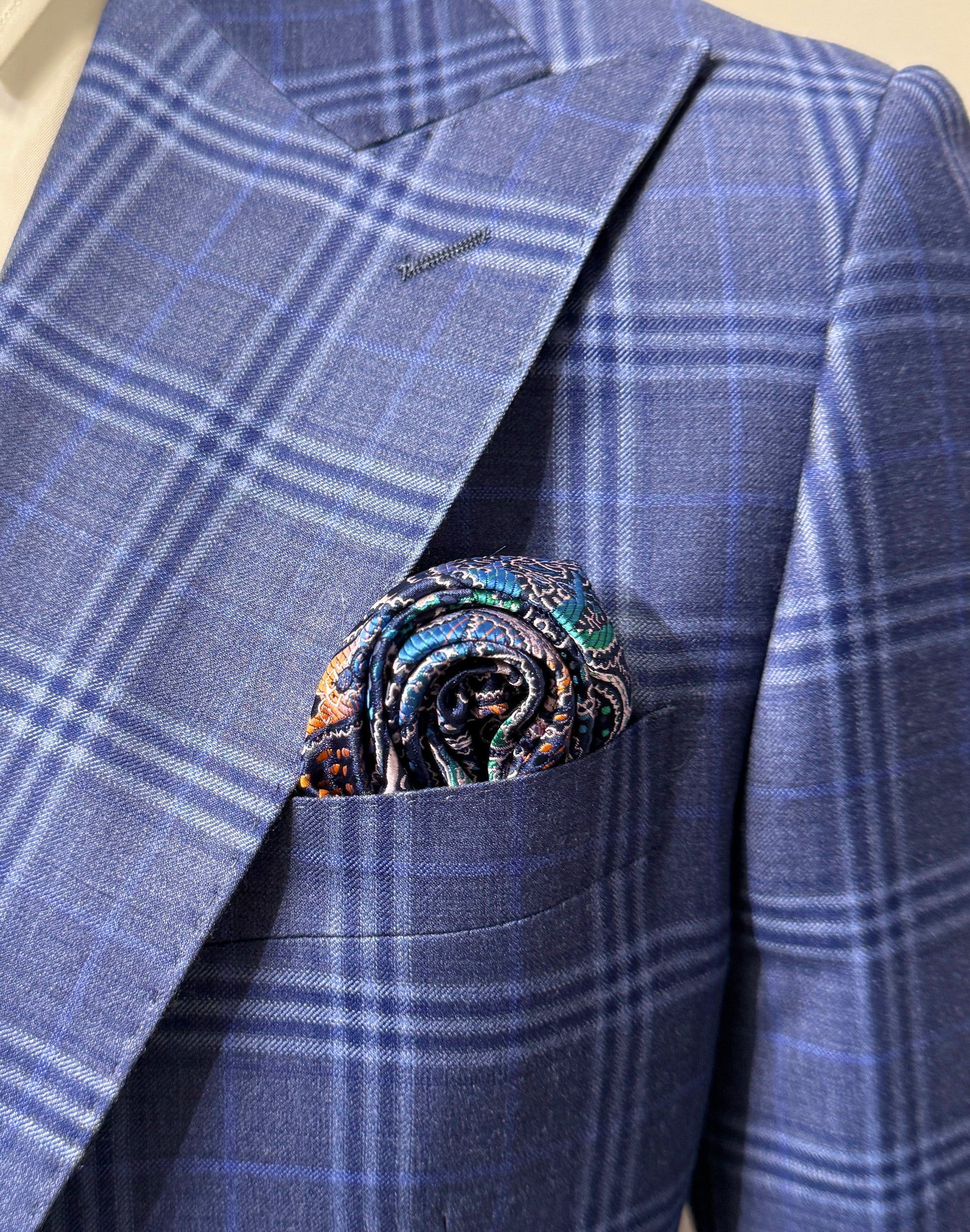 An older man in a Tiglio Rosso Orvietto Blue Plaid Semi Wide Leg suit (TL5074) with matching vest, white shirt, paisley tie, and pocket square stands against a plain white background.