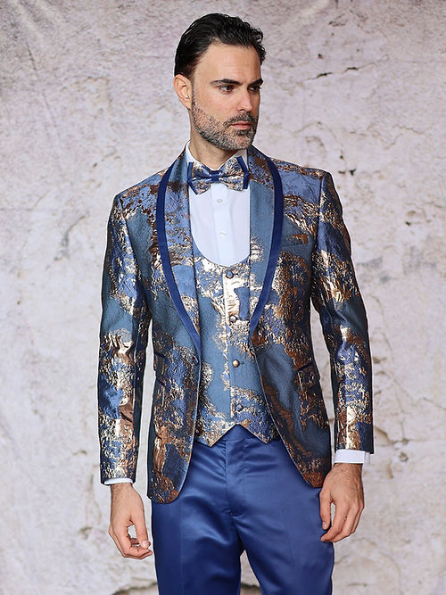 A man in an Insomnia MANZINI DELMAS slim-fit teal tuxedo with a shiny metallic pattern stands against a textured background, exuding elegance.