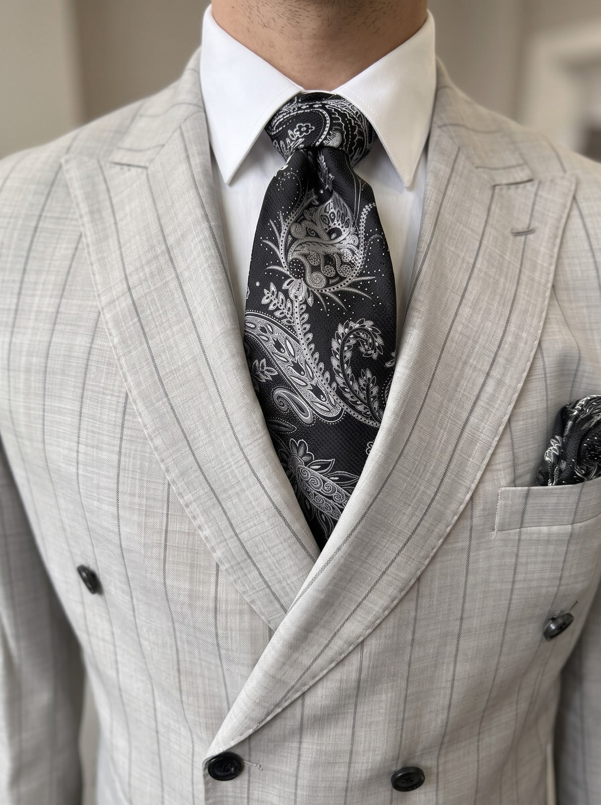 A man wearing a Tiglio Luxe PISTOIA Modern Fit Grey Pinstripe Double Breasted Suit WS8504 in light grey, styled with a white shirt and a dark patterned tie.