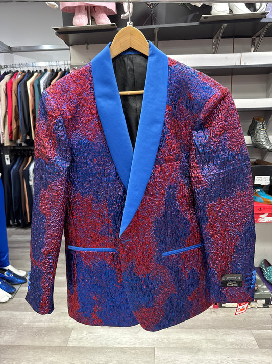 The EJ SAMUEL JACKET 3 CLEARANCE, featuring a red and blue crinkled pattern and a vibrant blue shawl collar, is displayed on a wooden hanger in the clothing store. Please note that this item is final sale—no returns or exchanges will be accepted.