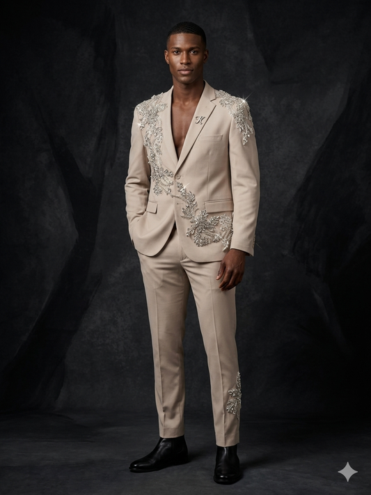 A man poses against a dark backdrop wearing the Unique Design Menswear custom prom suit in tan with clear stone detailing, paired with black dress shoes and no shirt under the blazer.