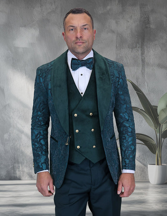 A man in the STATEMENT CLOTHING | EMPORIO-HUNTER by Statement Clothing—a slim fit green patterned shawl lapel tuxedo with matching velvet vest and bow tie—stands indoors near a potted plant, facing the camera.