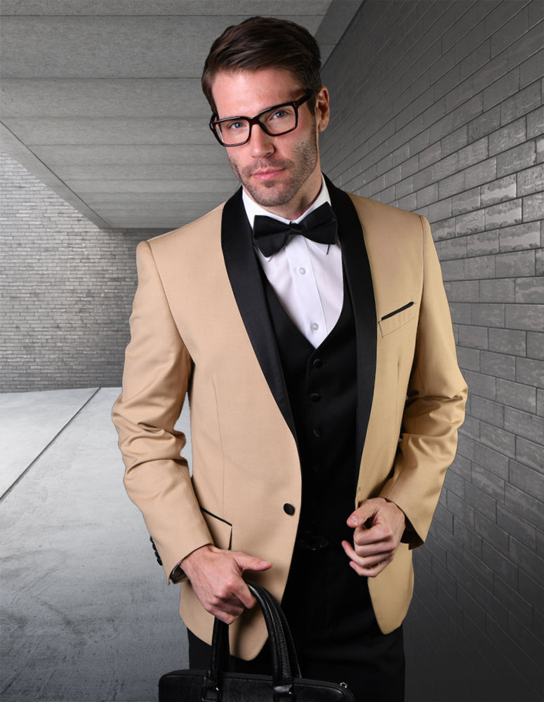 A man in Statement Clothing's ENCORE-CHAMPAGNE tuxedo with black lapels, tailored fit pants, white shirt, and black vest stands in a modern hallway holding a black bag.