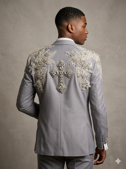 A man models the Custom prom suit by Unique Design Menswear, featuring grey silver rhinestones and a large cross on the back, standing against a plain gray background.