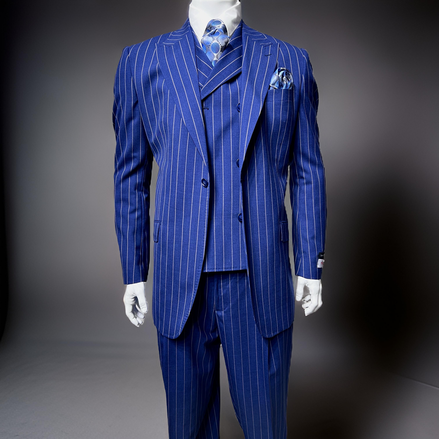 A mannequin showcases the Tiglio Rosso San Giovesse Blue/Camel Pinstripe suit (54R, 52L only) with matching trousers, a patterned blue tie, pocket square, and dress shirt. The wide-leg cut adds modern flair to this classic Tiglio Rosso look.