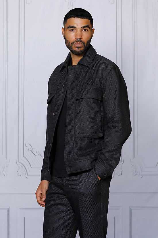 A man stands against a light-colored, paneled wall wearing the Insomnia INSOMNIA FENDI 2PC Black Leisure Suit.