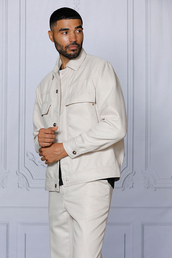 A man with short hair and a beard wears the INSOMNIA FENDI 2PC Tan Leisure Suit by Insomnia, featuring large front pockets, standing against a light-paneled background.